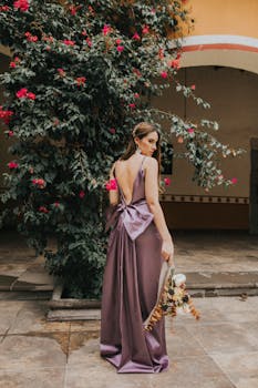 一位身着紫色礼服的时尚女士，在花卉背景前手持花束摆出姿势，非常适合时尚优雅的主题