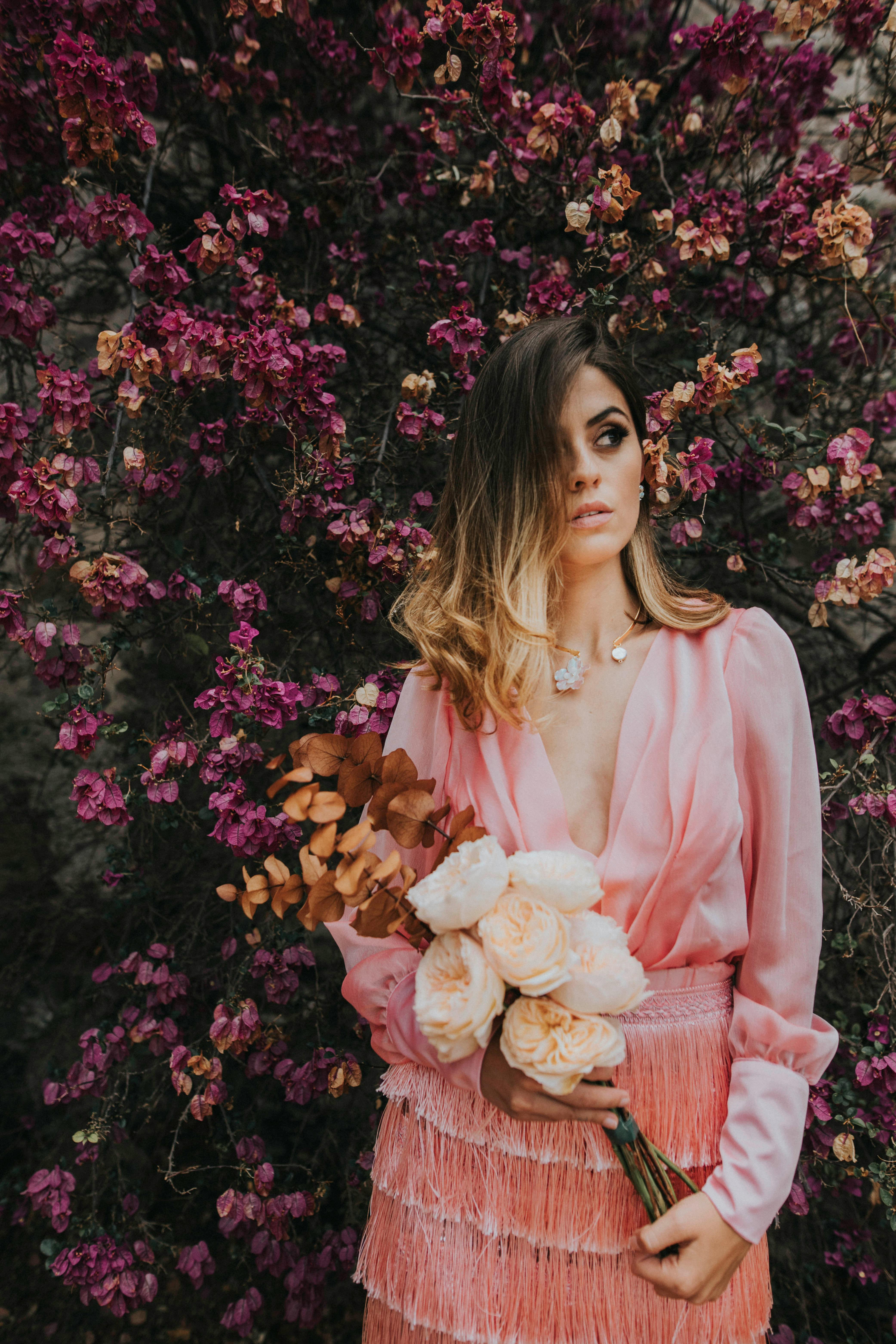 Stylish woman in a pink outfit stands elegantly with flowers, creating a blend of fashion and nature.