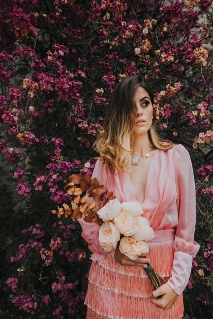 Stylish woman in a pink outfit stands elegantly with flowers, creating a blend of fashion and nature.