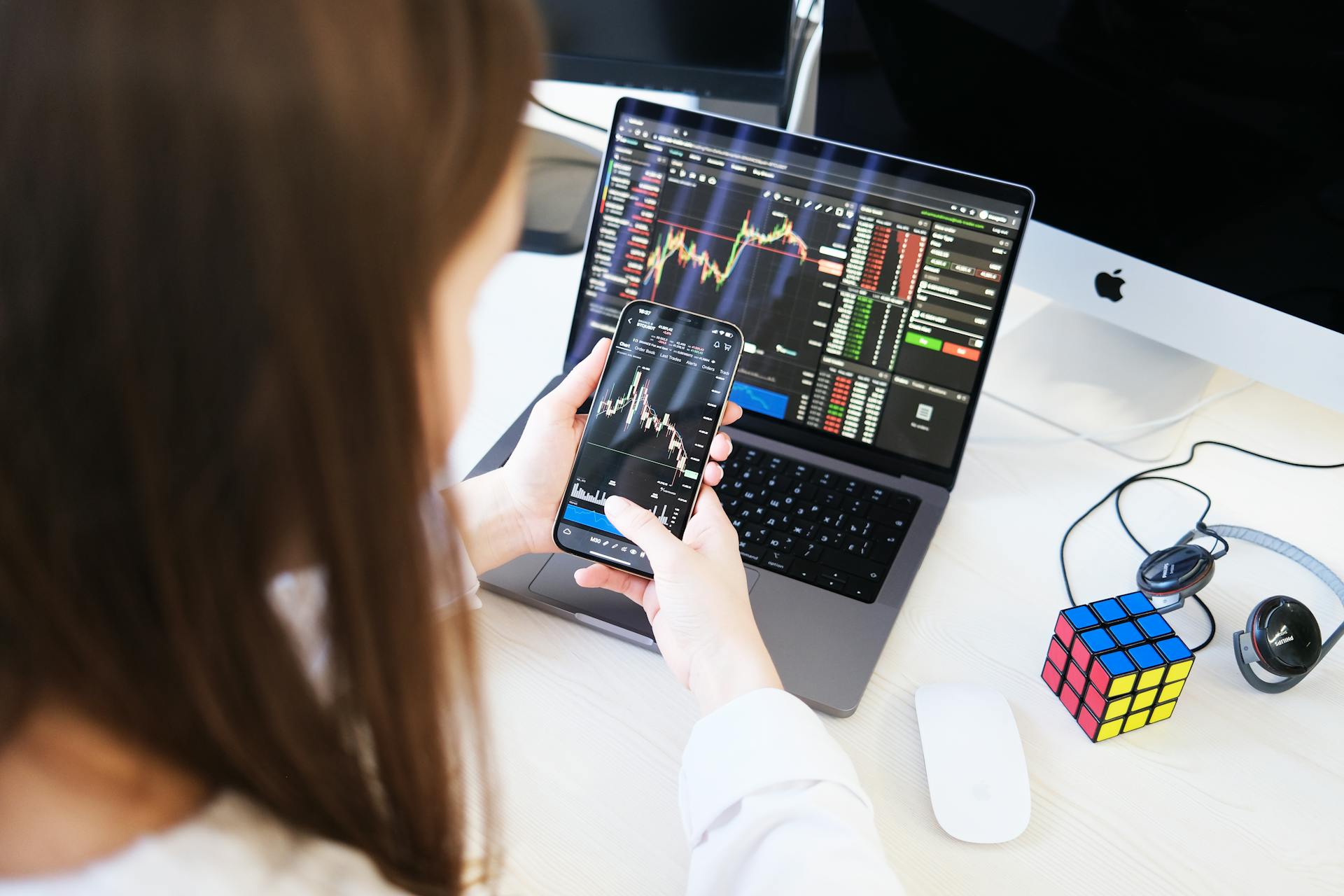 A Woman Looking at Cryptocurrency Charts on Her Smartphone and Laptop