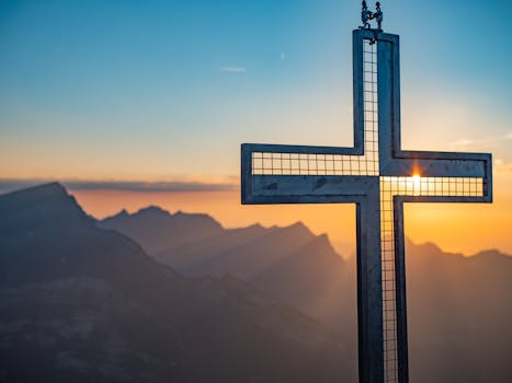 A cross silhouetted against a vibrant sunset over mountain peaks in Glarus, Switzerland.