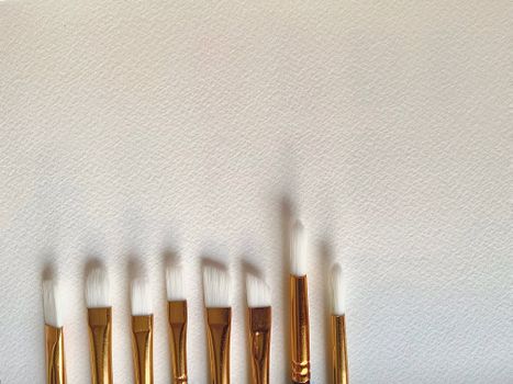 Top view of a set of gold handle paintbrushes arranged on a white textured canvas.