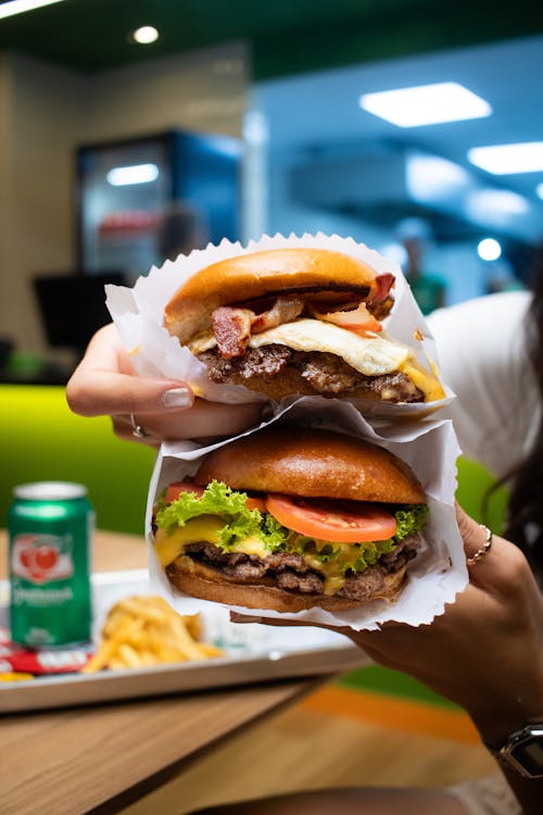 A person holding two hamburgers with fries and soda