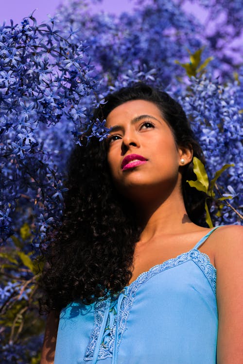 Low Angle Photo of Woman Standing Near Blue-Petaled Flowers