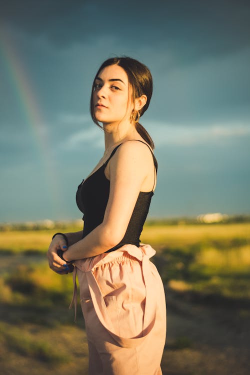 Side View Photo of Woman in Black Spaghetti Strap Top and Pink Dungarees Standing Outside Posing