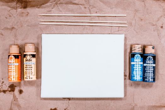 Top view of acrylic paints and blank canvas with brushes on kraft paper background.