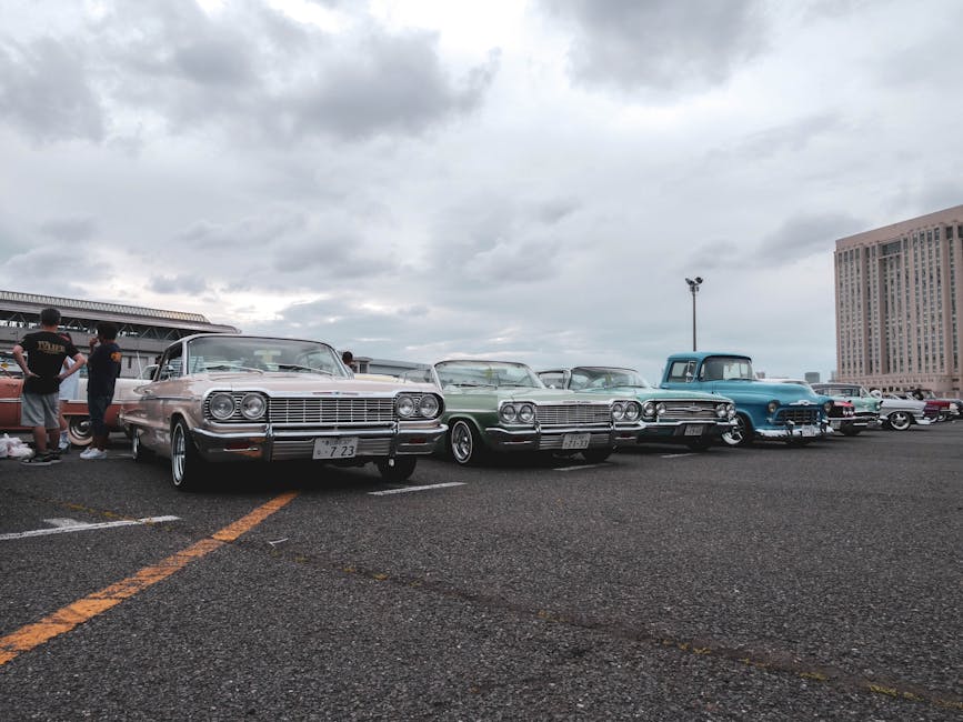 Vintage cars in a parking lot under a cloudy sky, showcasing a classic car meetup.