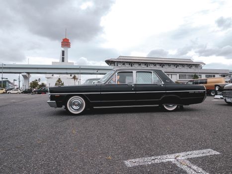 Vintage black car parked outdoors with a tower in the background under cloudy skies.