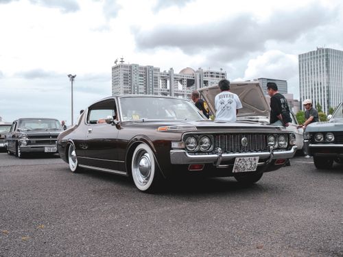 Free Classic cars displayed at a meetup with buildings in the background and enthusiasts gathered around. Stock Photo