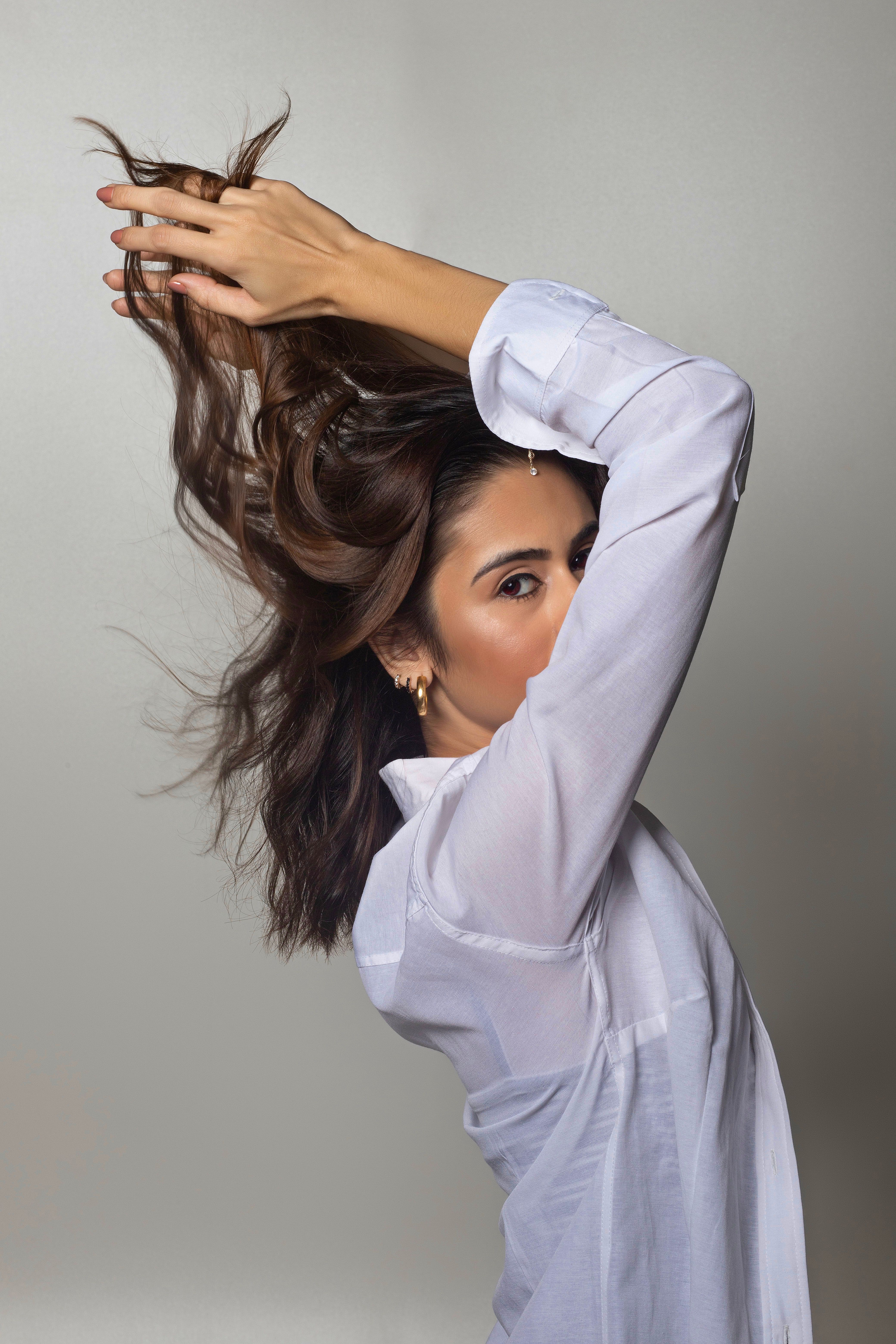 Portrait of a woman in a studio setting, elegantly posing with flowing brown hair and wearing a white shirt.
