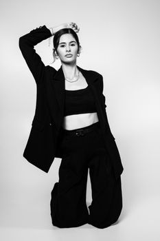 Sophisticated black and white portrait of a woman in stylish attire kneeling, exuding modern elegance.