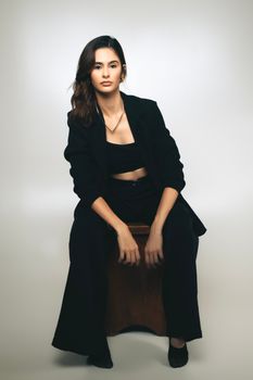 Portrait of a woman in chic black suit posing confidently in a studio setting.