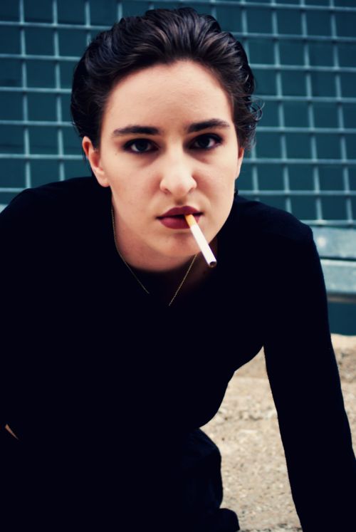 Free Moody portrait of a woman with red lips holding a cigarette. Urban setting. Stock Photo