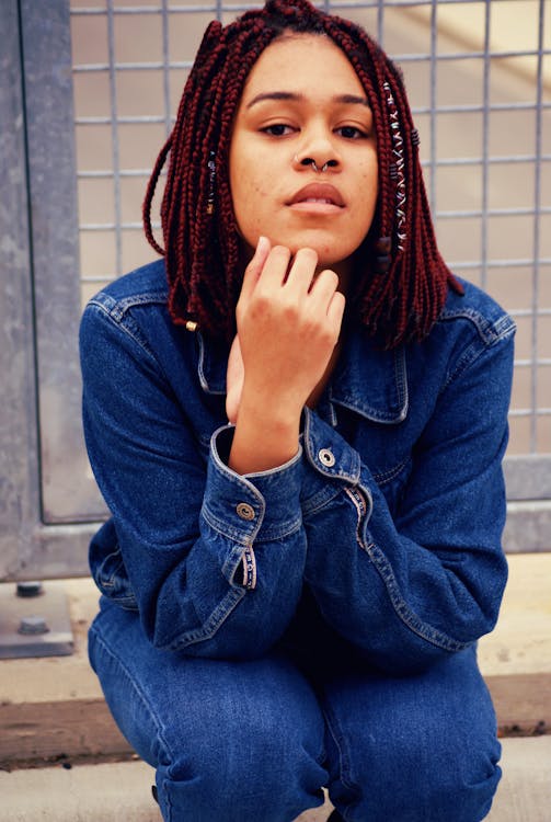 Photo of Woman in Blue Denim Outfit Sitting on Concrete Surface In Front of Metal Fence