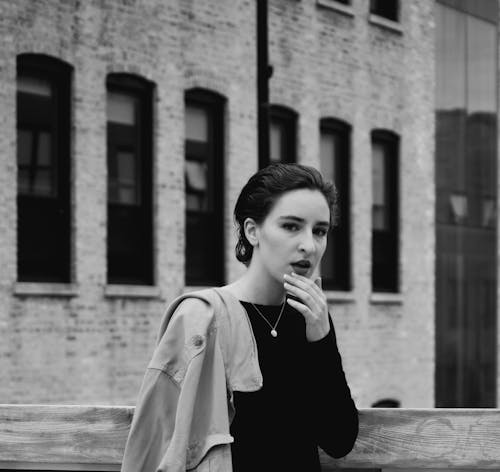 Grayscale Photography of Woman  Holding Chin Beside a Building