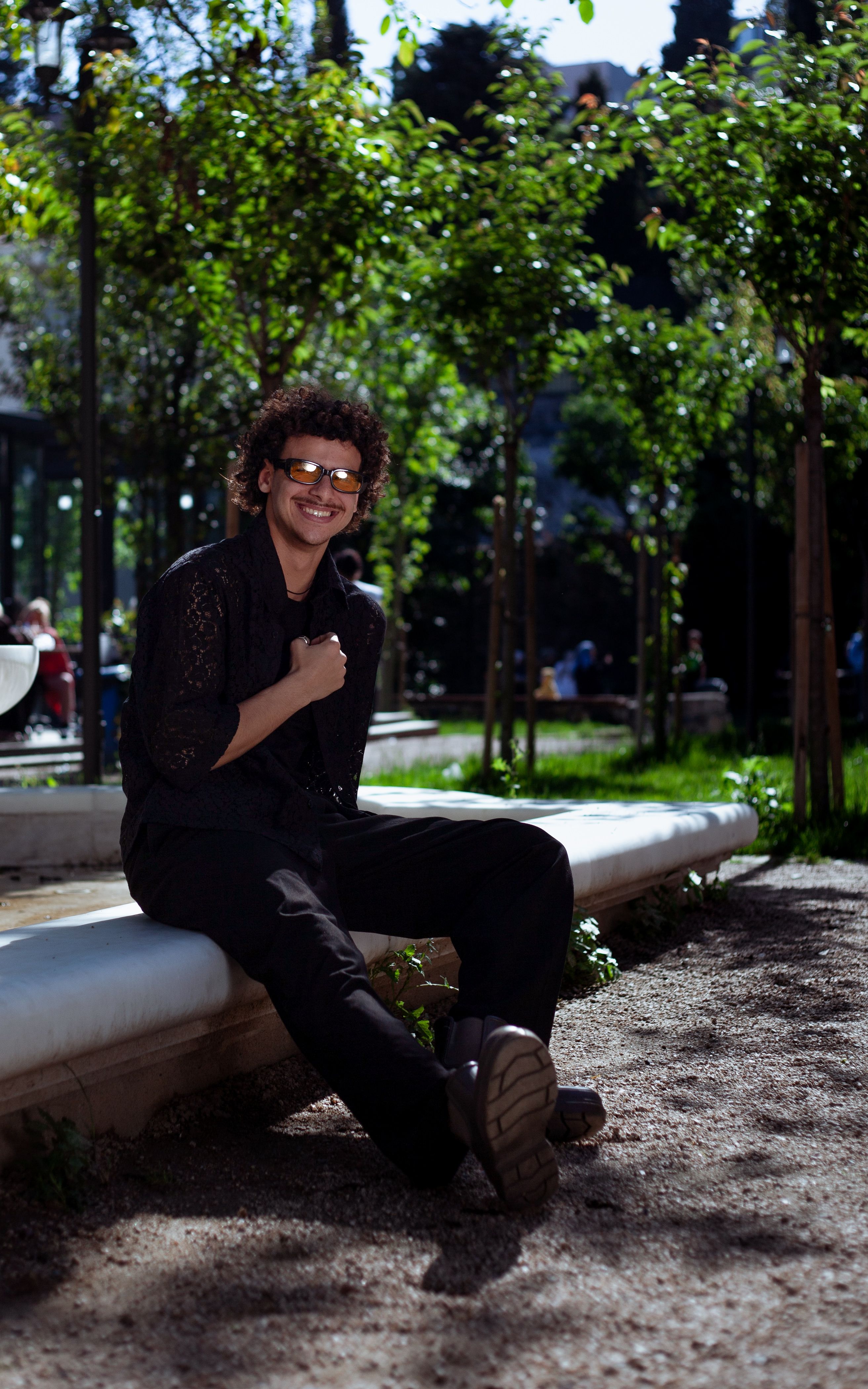 Casual portrait of a young man in sunglasses smiling in a sunny urban park.