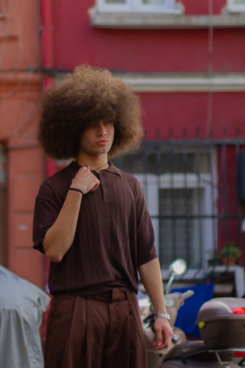 Free Portrait of a man with afro hair wearing a brown polo shirt, standing in an urban environment. Stock Photo