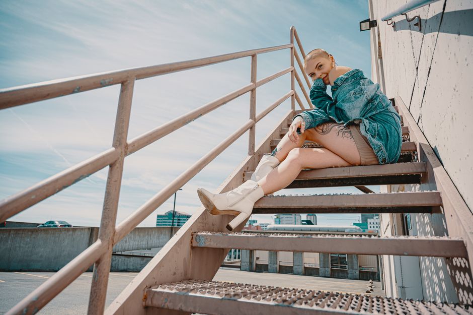 Fashionable woman in denim posing on outdoor stairway in sunny urban setting, showcasing style and confidence.