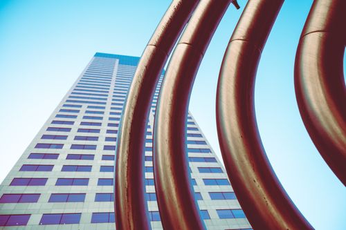 Free A low-angle view of a modern skyscraper and futuristic metal sculpture against a blue sky. Stock Photo