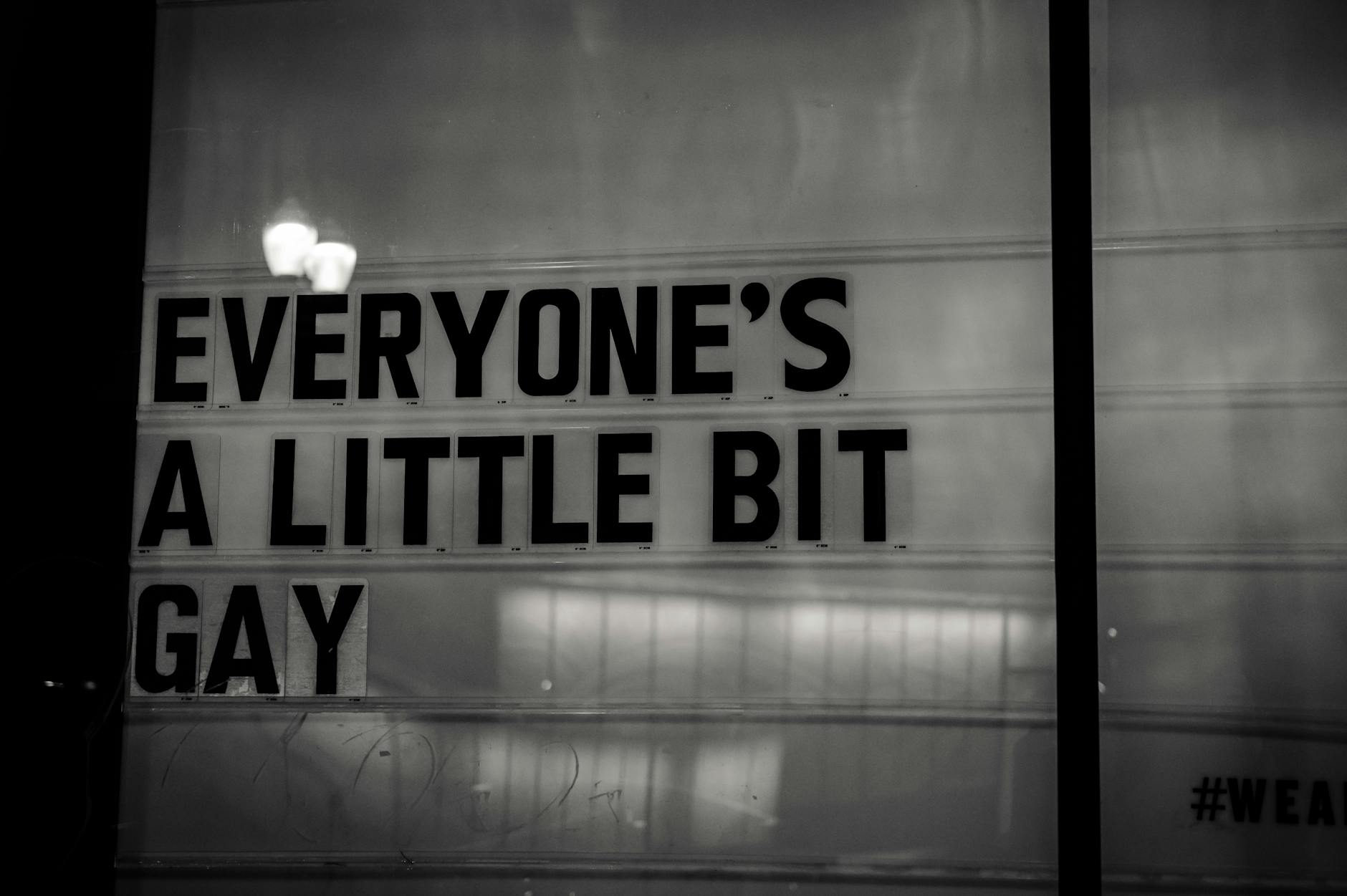 تطبيق TAIMI – للمواعدة والدردشة الآمنة لمجتمع LGBTQ+ مع مميزات سهلة الاستخدام Black and white photo of a sign reading 'Everyone's a little bit gay', promoting inclusivity.