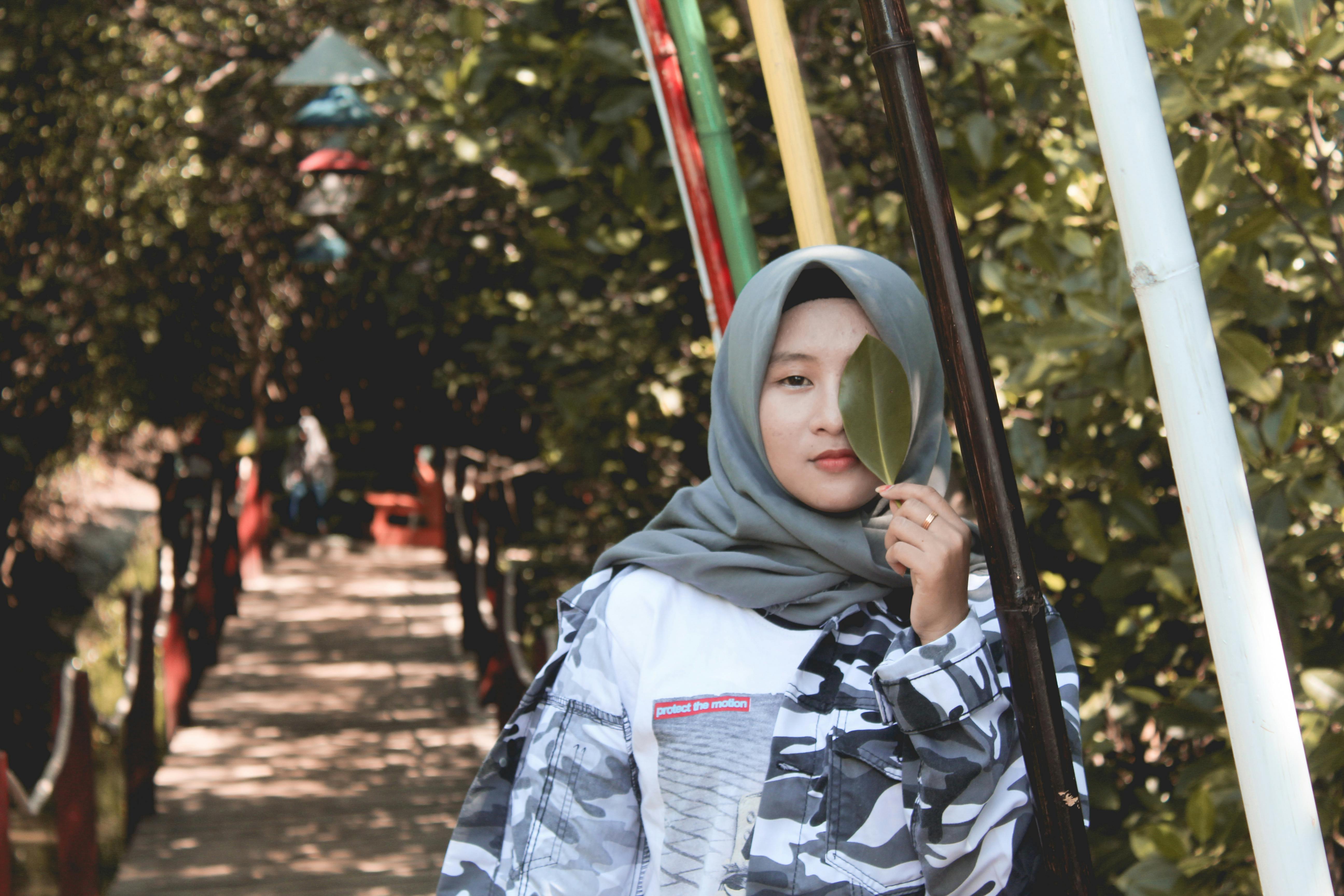 一位时尚女子戴着头巾站在户外，手拿一片叶子，拥抱大自然