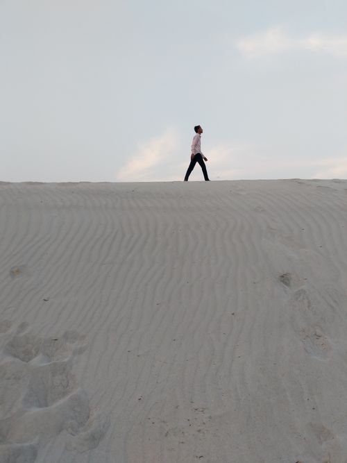 Free Silhouette of a person walking atop a vast sandy dune under a soft morning sky. Stock Photo