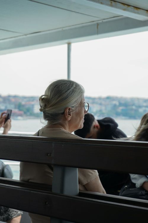 Free Senior woman with glasses sits on a ferry, enjoying city views as it passes through urban waters. Stock Photo