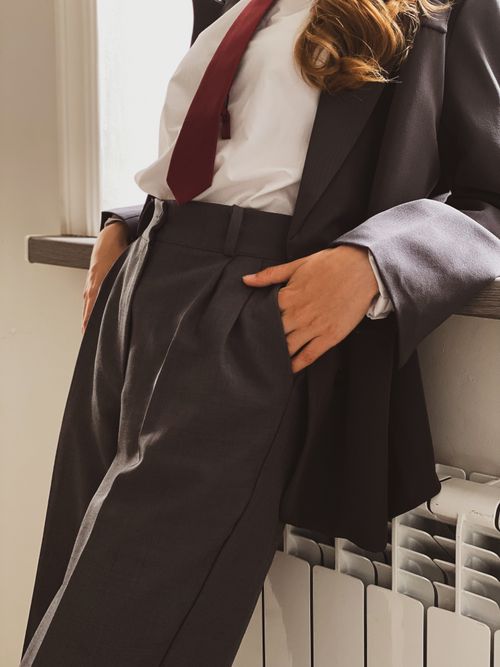 Free Fashion-forward businesswoman in a suit and tie, confidently leaning indoors for a modern professional look. Stock Photo