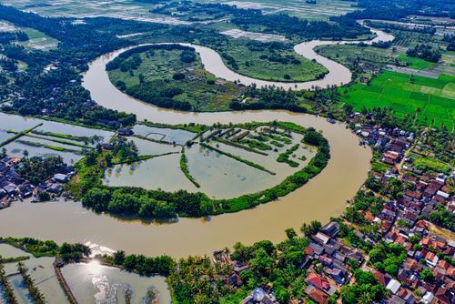 Free Aerial view capturing the vibrant landscape of a meandering river surrounded by green fields and houses. Stock Photo