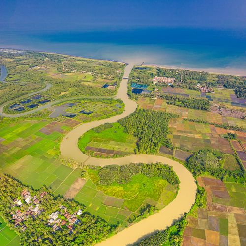 Free A breathtaking aerial view of lush farmland, meandering river, and coastal areas under a clear blue sky. Stock Photo