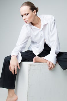 Stylish woman in white shirt and black pants seated on a block, showcasing elegance and fashion.