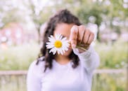 在宁静的户外环境中，一名妇女专注地拿着一朵白雏菊