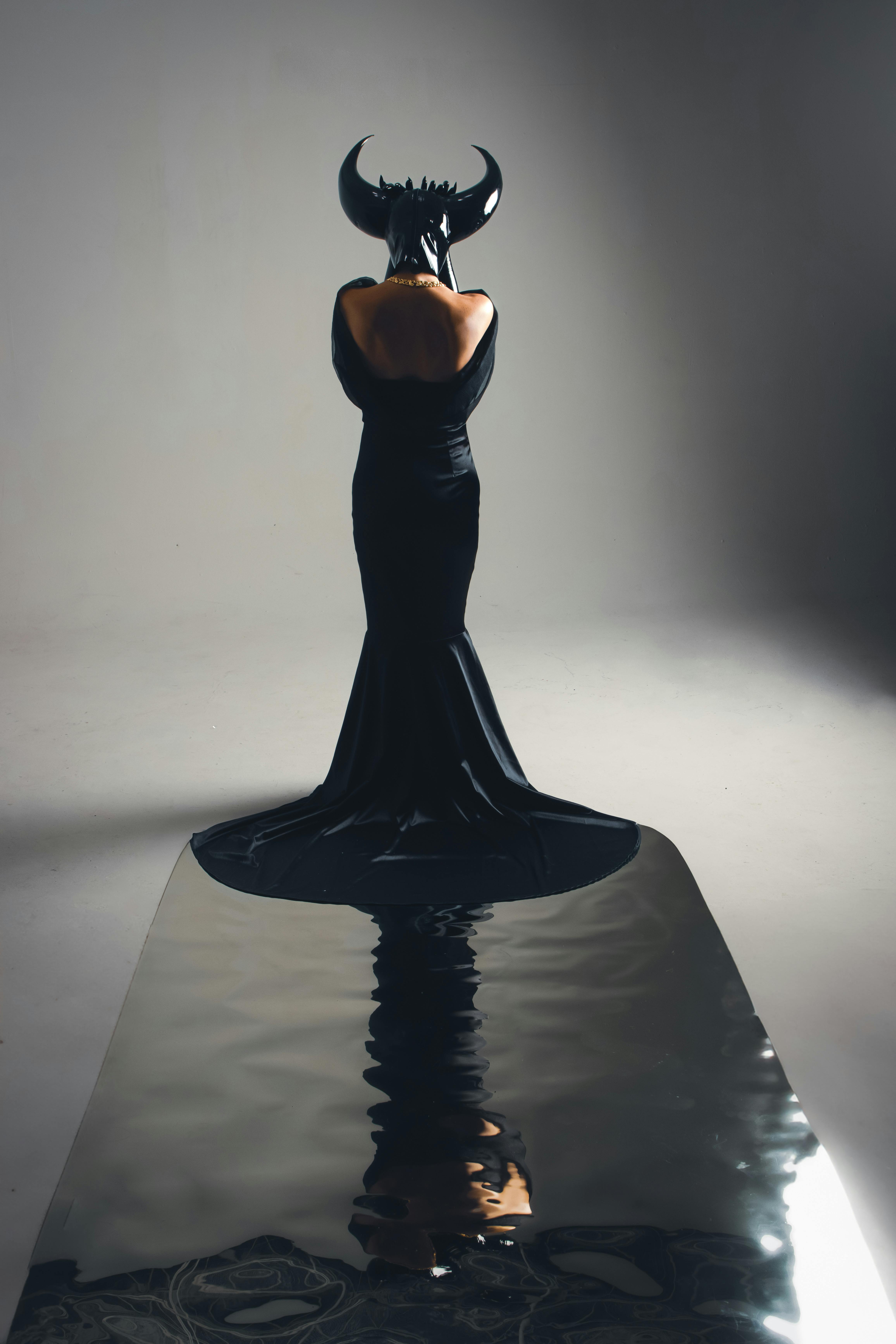 Ücretsiz Siyah bir elbise ve boynuzlu bir başlık giyen bir kadın, minimalist bir ortamda sanatsal bir şekilde duruyor. Stok Fotoğraflar