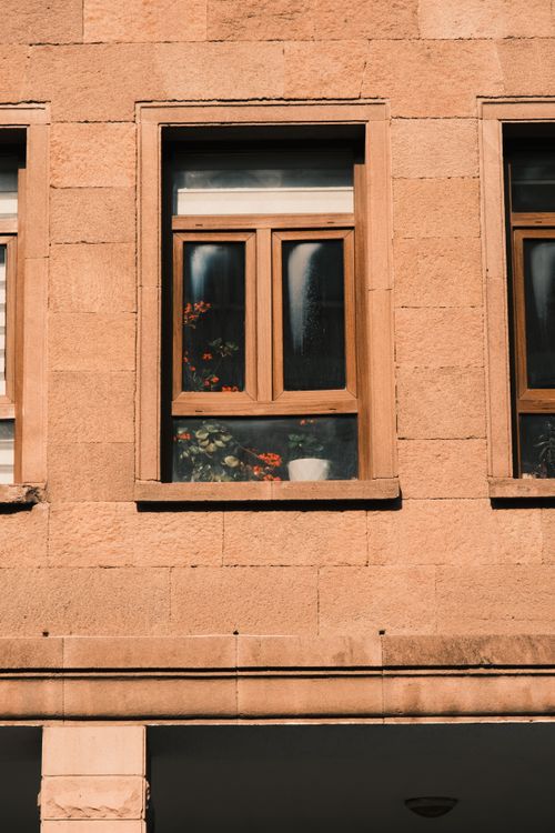 Free Close-up of a rustic stone building facade with wooden framed windows and potted flowers. Stock Photo