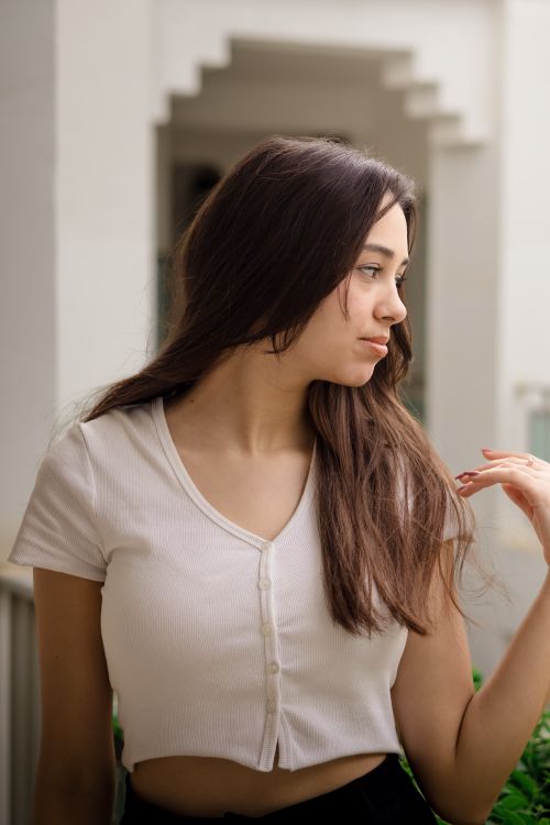 Free Stylish portrait of a woman with long hair, wearing a white blouse against a neutral background. Stock Photo