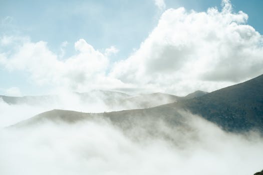 Breathtaking view of foggy mountains under a bright, cloud-filled sky.
