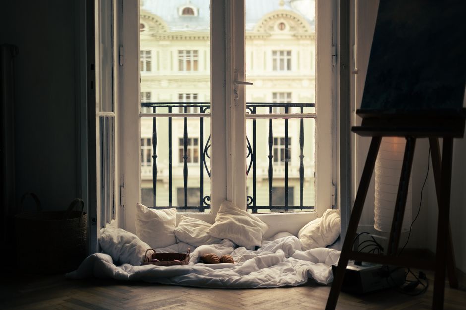 A cozy indoor scene with pillows by a balcony window, overlooking classic architecture.
