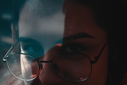 Free Close-up view of a woman's face with eyeglasses reflected in a window light. Stock Photo