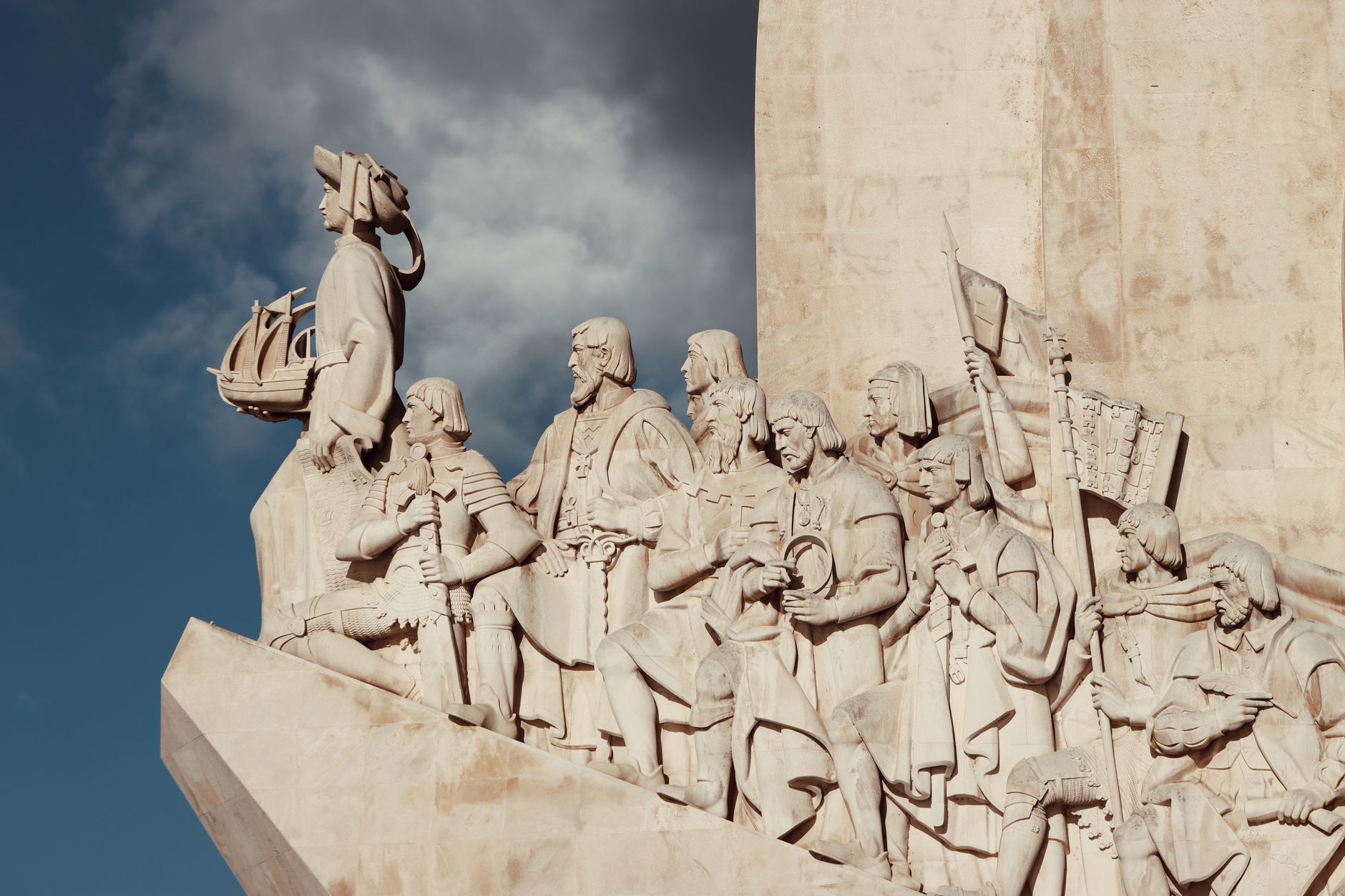 Close-up view of the Monument of Discoveries in Lisbon, Portugal with intricate stone carvings against a vibrant blue sky.