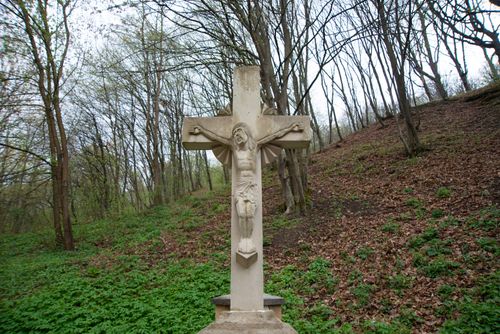 Free A stone crucifix depicting Jesus stands amidst a peaceful forest hillside, symbolizing faith and tranquility. Stock Photo
