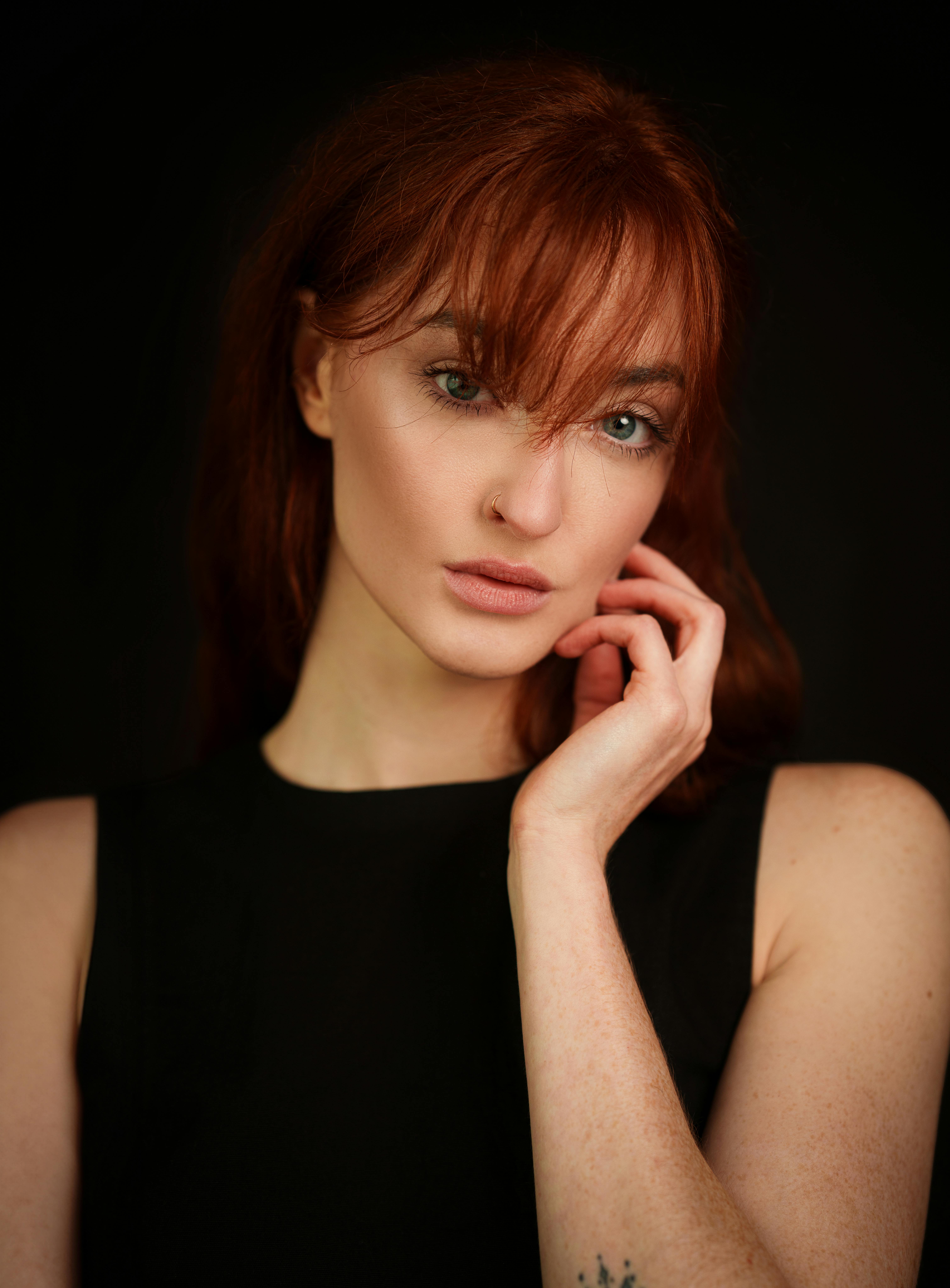 Studio portrait of a serene redhead woman posing against a black background, showcasing elegance and beauty.