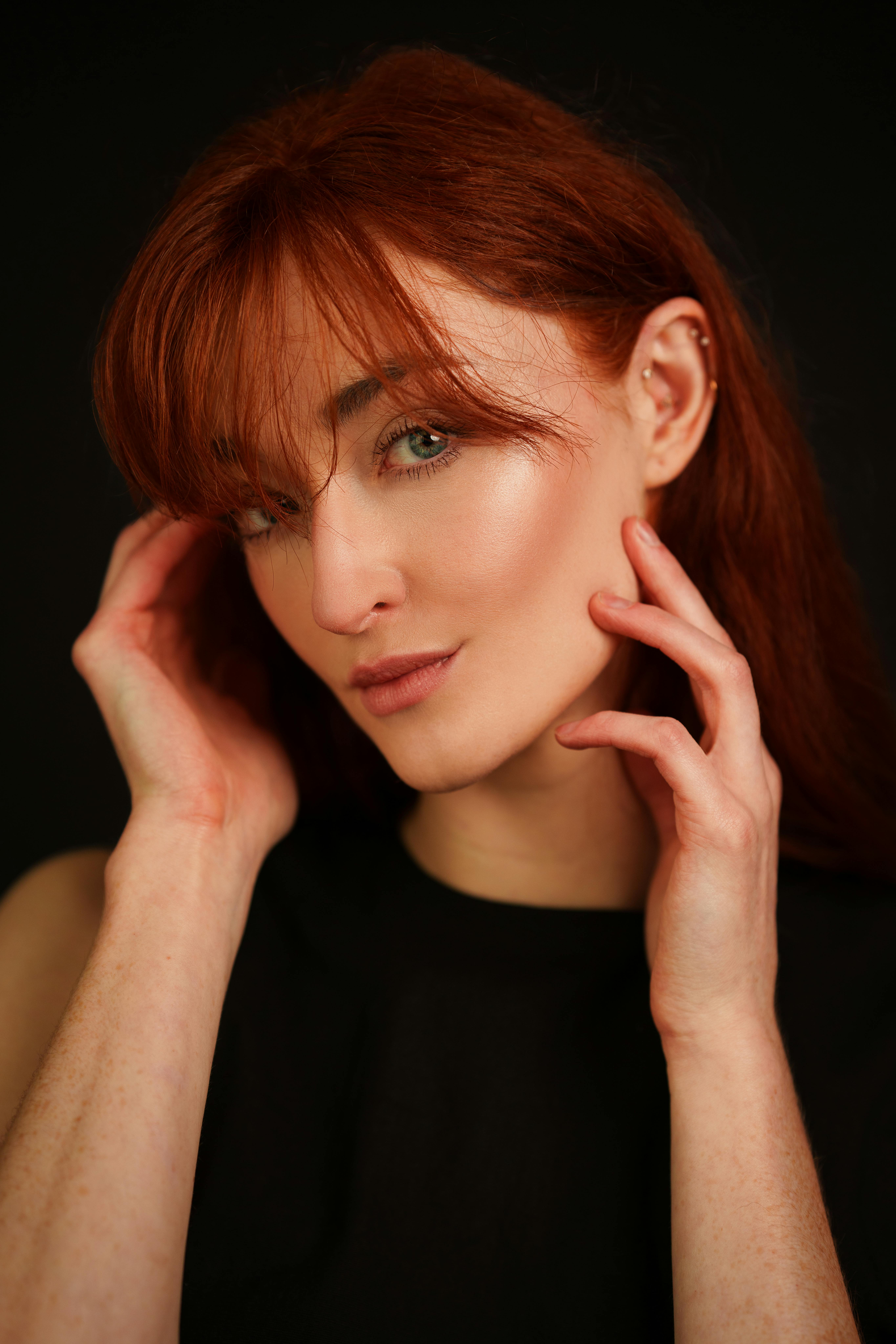 A captivating studio portrait of a redhead woman with a gentle smile and thoughtful expression.