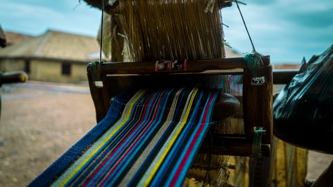 Close-up of a traditional handloom weaving a colorful textile in a rural setting.