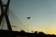 日落时分，一架无人机的剪影在现代斜拉桥附近飞行