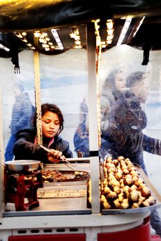 Woman grilling chestnuts at an open-air market booth, with smoky atmosphere and winter vibe.