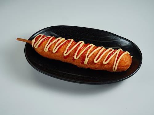A hot dog with sauce on it on a black plate