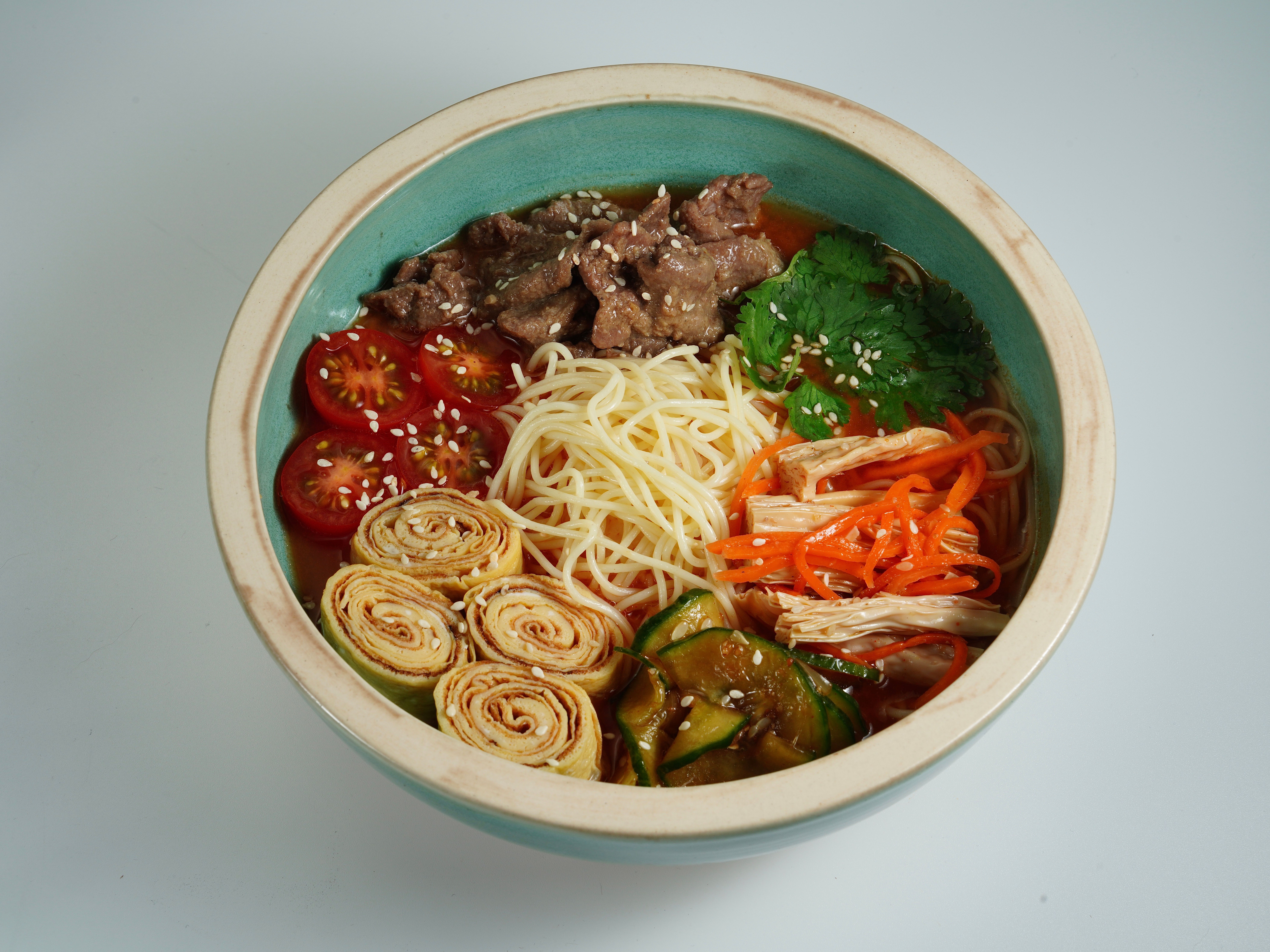 Colorful Asian noodle bowl featuring fresh veggies, beef, and noodles garnished with herbs and sesame.