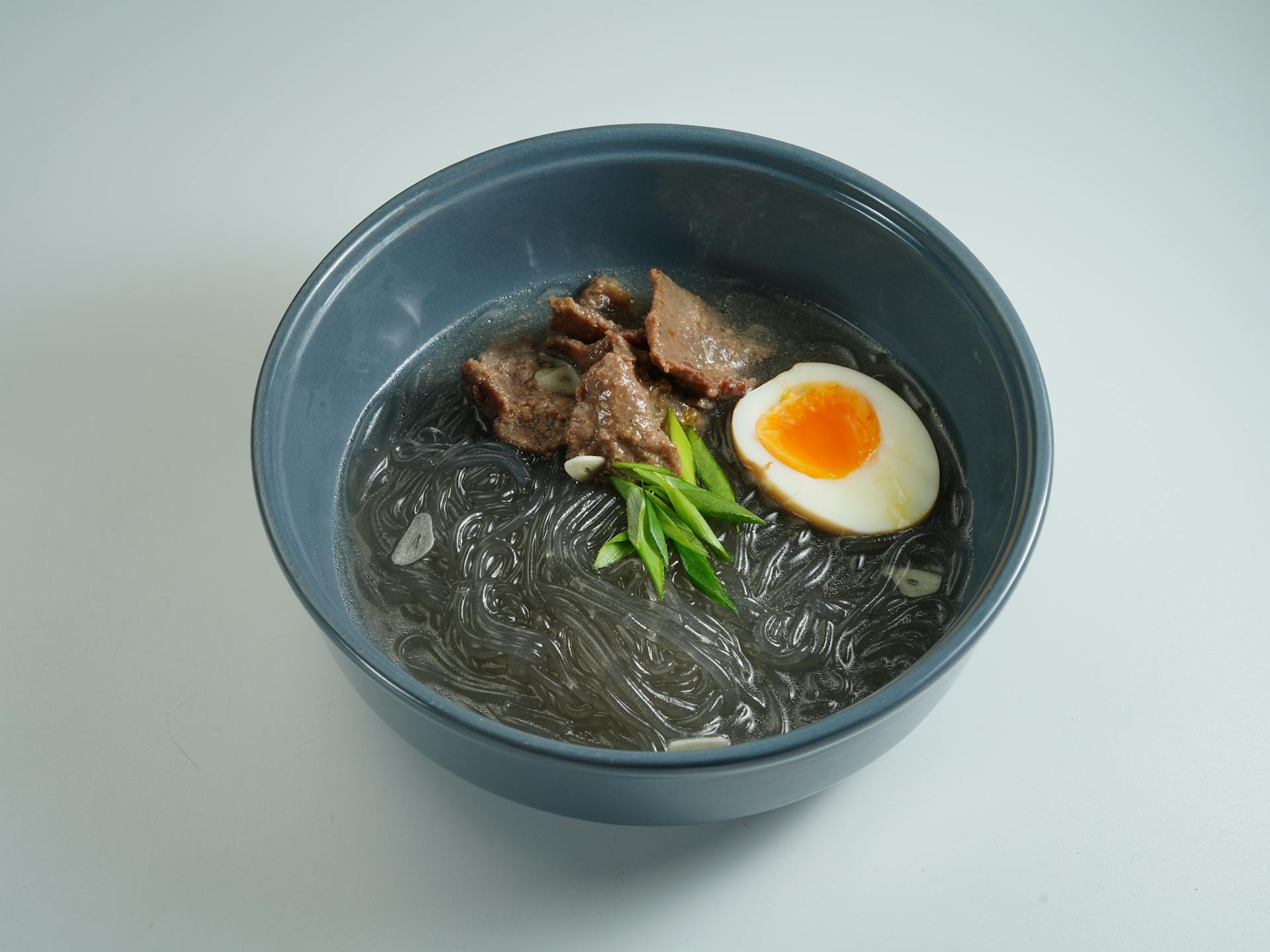 Delicious bowl of Asian glass noodle soup with beef slices, boiled egg, and fresh scallions.