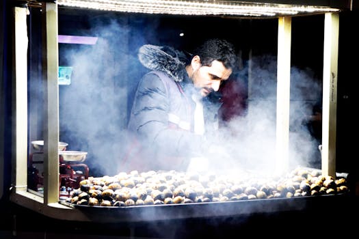 Man selling roasted chestnuts in a smoky street food stall at night.