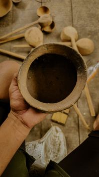 A craftsman holding a rustic, handmade clay bowl with wooden ladles in the background. - Fotografer Sidoarjo